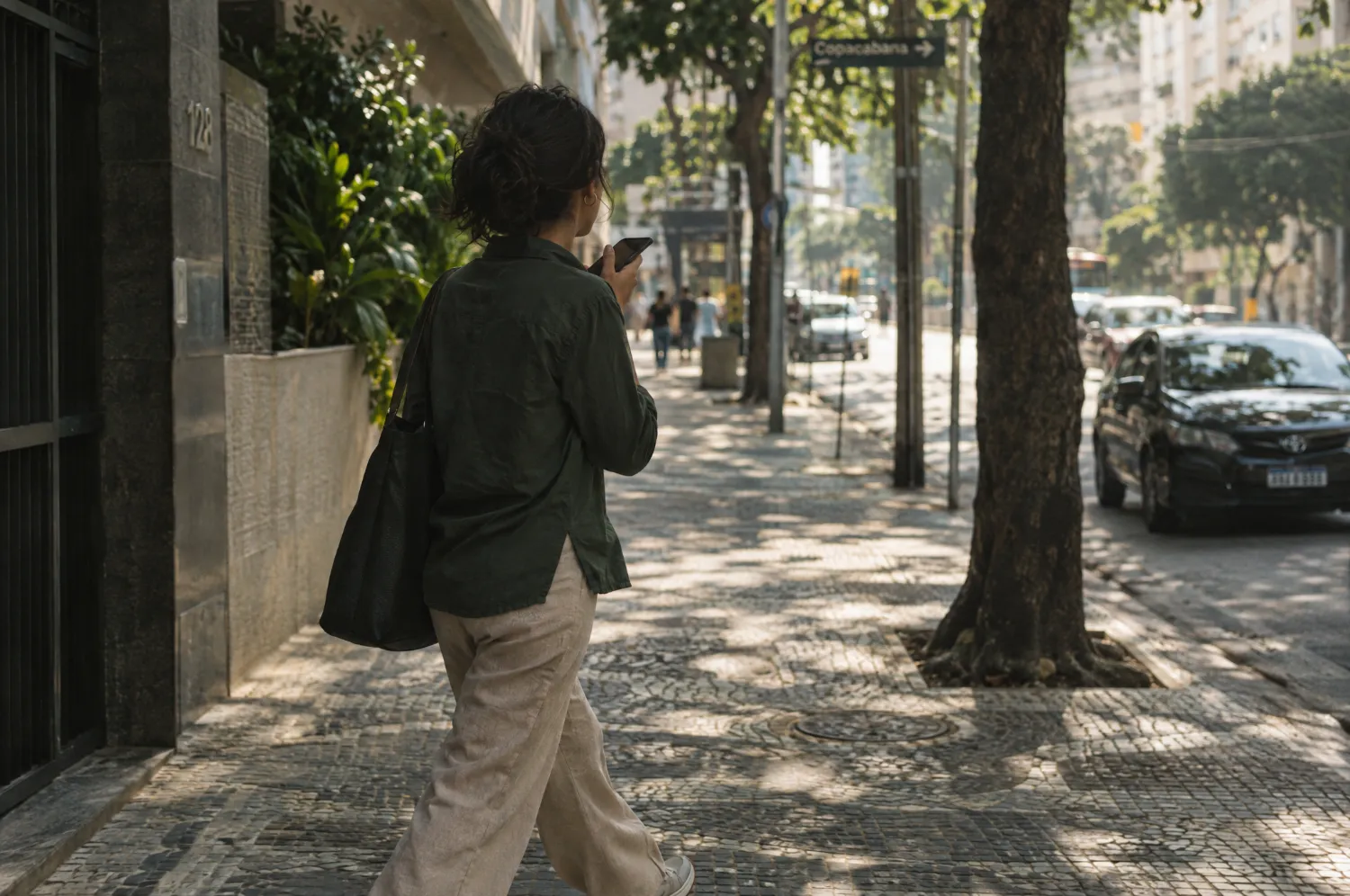 Pessoa caminhando por uma calçada, falando ao celular junto ao peito.